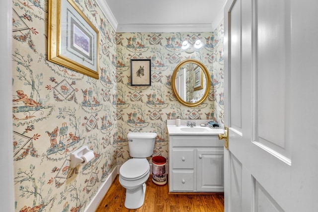 half bathroom with wallpapered walls, toilet, wood finished floors, crown molding, and vanity