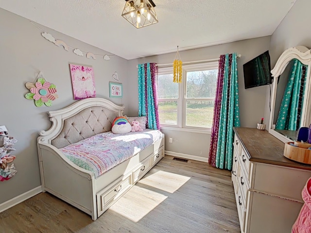 bedroom with light wood-type flooring, visible vents, baseboards, and a textured ceiling