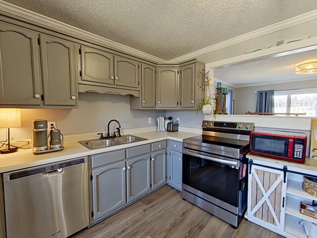 kitchen featuring stainless steel appliances, wood finished floors, a sink, light countertops, and crown molding