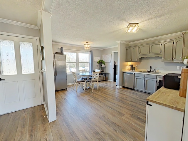 kitchen featuring crown molding, stainless steel appliances, light countertops, light wood-style flooring, and a sink