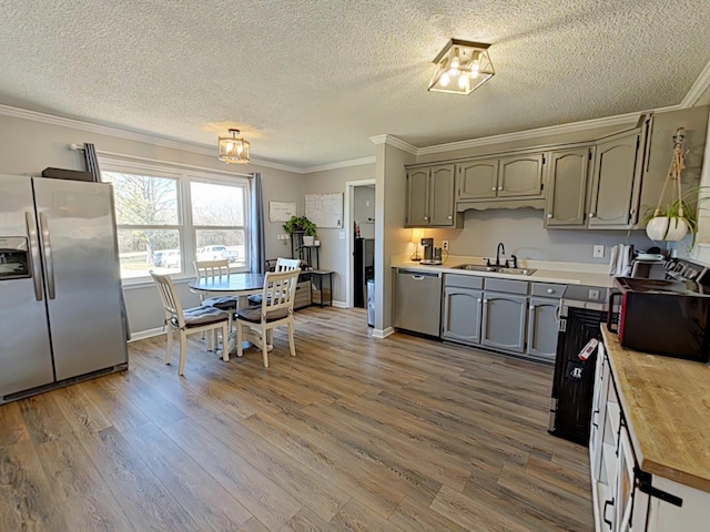 kitchen featuring butcher block counters, appliances with stainless steel finishes, wood finished floors, crown molding, and a sink