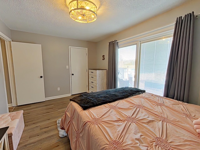 bedroom featuring access to exterior, a textured ceiling, baseboards, and wood finished floors