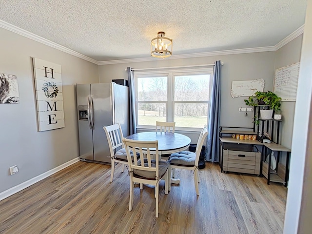 dining area featuring light wood-type flooring, baseboards, ornamental molding, and a textured ceiling