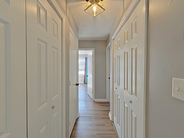 hall with light wood-style flooring, baseboards, and a textured ceiling