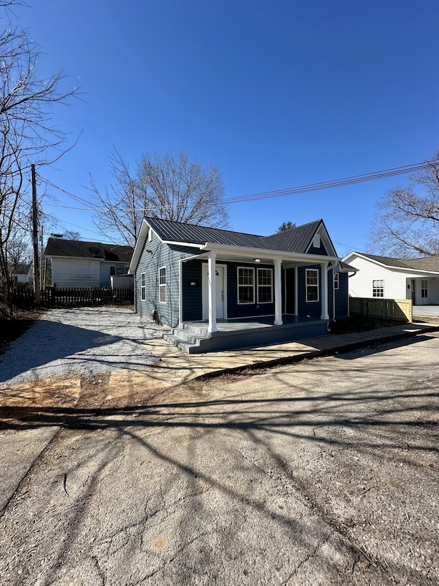 view of front facade featuring driveway, covered porch, fence, and metal roof