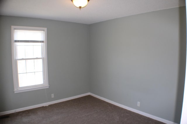 spare room with dark colored carpet, plenty of natural light, and baseboards