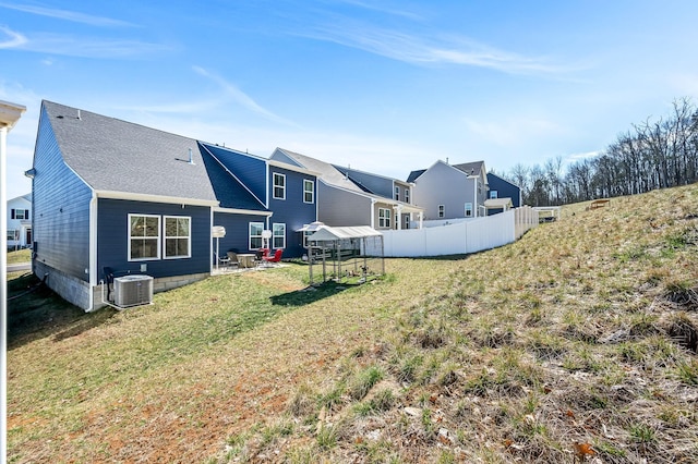 rear view of property with a shingled roof, a lawn, fence, and central air condition unit