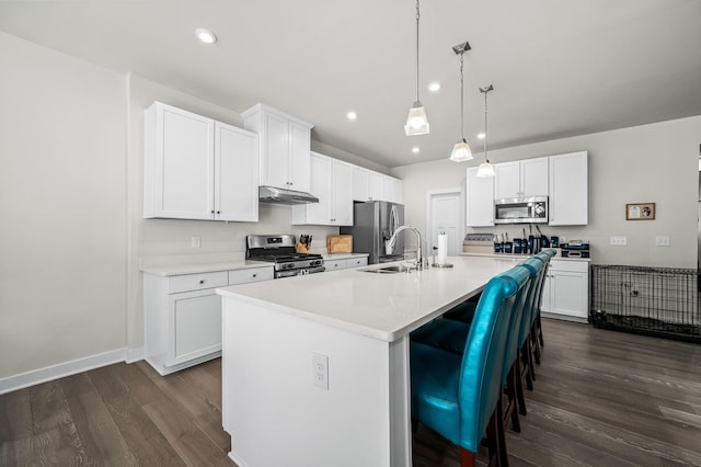 kitchen featuring dark wood-style floors, appliances with stainless steel finishes, a kitchen island with sink, a sink, and under cabinet range hood