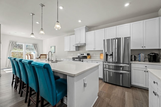 kitchen featuring dark wood finished floors, stainless steel appliances, light countertops, under cabinet range hood, and a sink