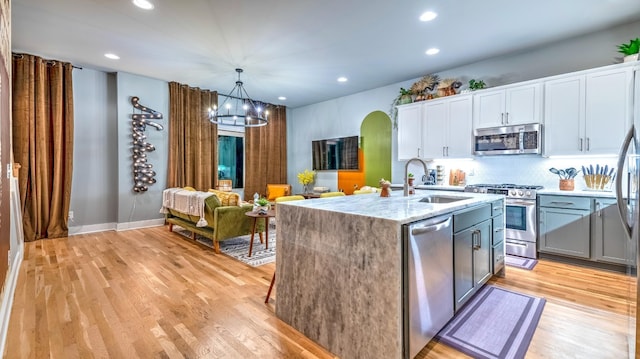 kitchen with arched walkways, appliances with stainless steel finishes, light wood-style floors, white cabinetry, and a sink