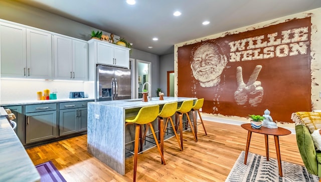 kitchen with stainless steel fridge with ice dispenser, light wood-style flooring, a breakfast bar, light countertops, and a sink