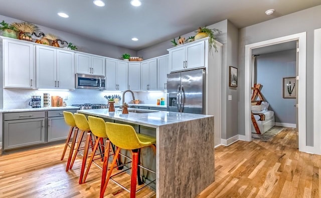 kitchen featuring appliances with stainless steel finishes, a kitchen breakfast bar, a kitchen island with sink, light wood-style floors, and a sink