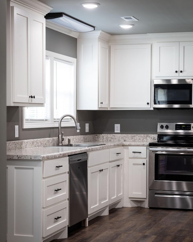 kitchen with dark wood finished floors, white cabinetry, stainless steel appliances, and a sink