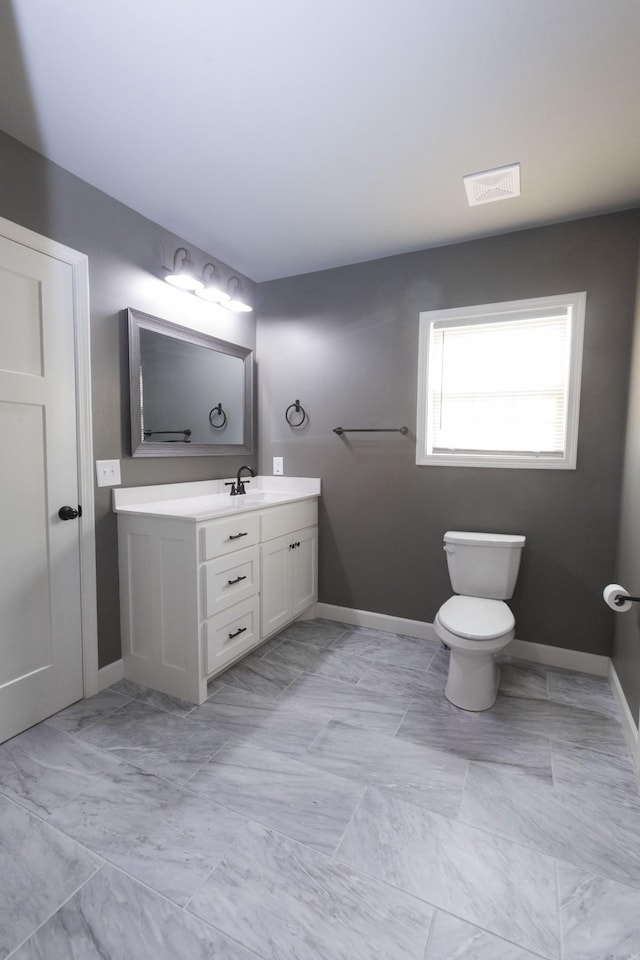 bathroom featuring toilet, vanity, visible vents, and baseboards