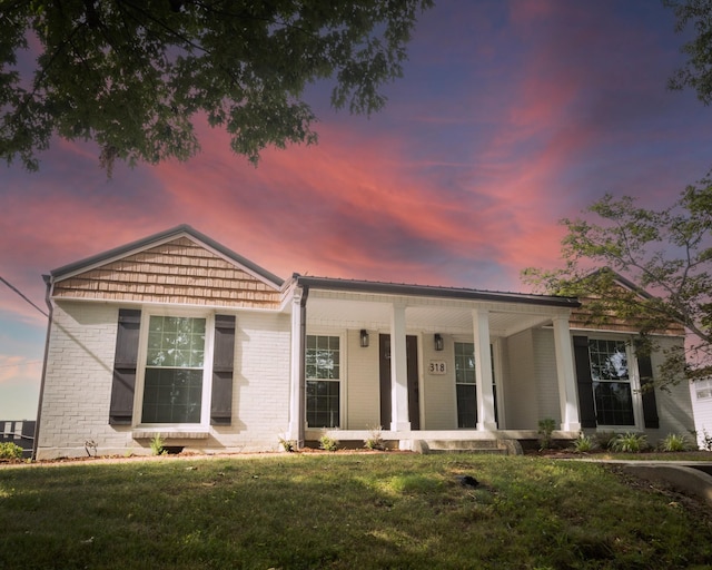 view of front facade with covered porch, a front lawn, and brick siding