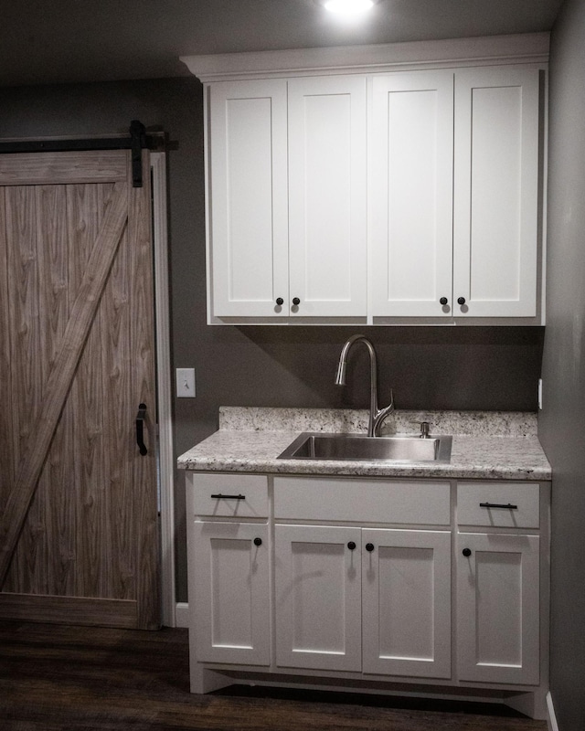 kitchen with light stone countertops, white cabinets, a sink, and a barn door