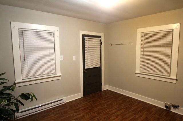 empty room featuring dark wood-style flooring, a baseboard radiator, and baseboards