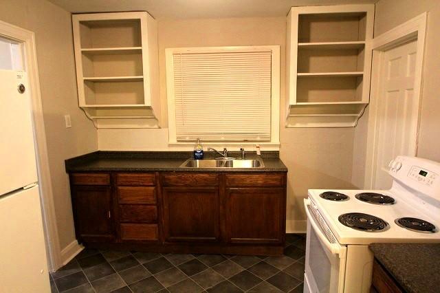 kitchen with dark countertops, white appliances, open shelves, and a sink