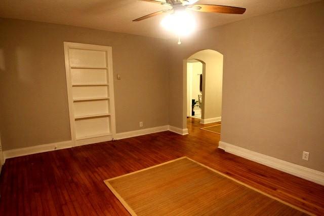 unfurnished room featuring built in shelves, arched walkways, ceiling fan, wood finished floors, and baseboards