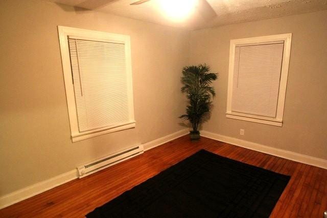 spare room with a ceiling fan, baseboards, a baseboard heating unit, and wood finished floors