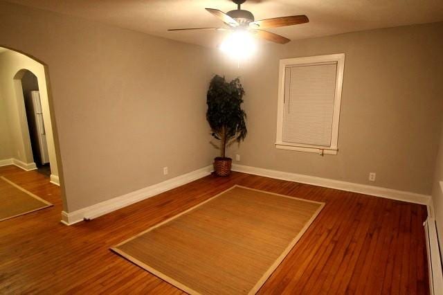 spare room featuring a ceiling fan, arched walkways, baseboards, and wood finished floors