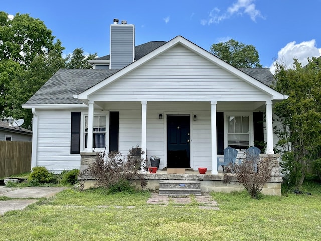 bungalow with a chimney, roof with shingles, covered porch, fence, and a front lawn