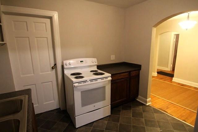 kitchen featuring arched walkways, white electric stove, dark countertops, a sink, and baseboards