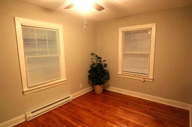 unfurnished room featuring a ceiling fan, a baseboard radiator, dark wood-style flooring, and baseboards