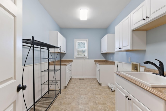 laundry area featuring light tile patterned floors, washer hookup, a sink, wainscoting, and cabinet space