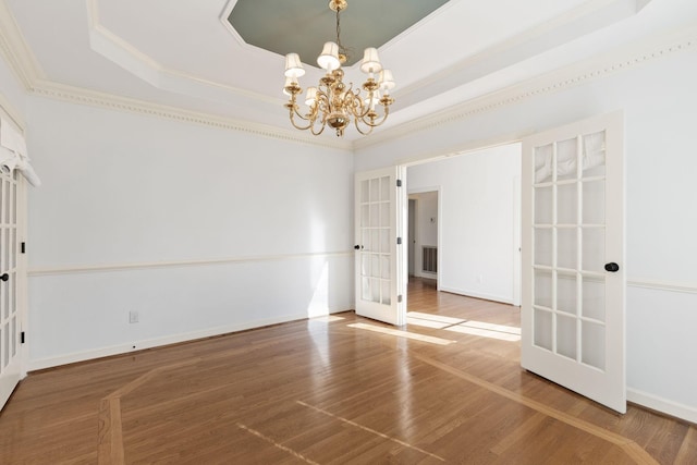 spare room featuring baseboards, a raised ceiling, wood finished floors, french doors, and a notable chandelier