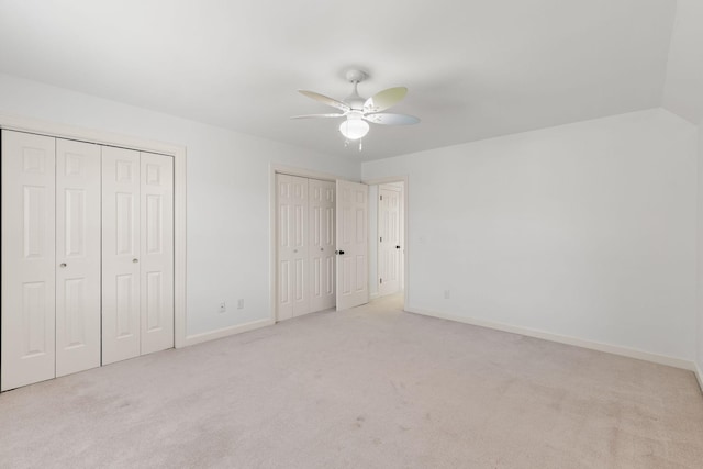 unfurnished bedroom with two closets, a ceiling fan, carpet flooring, vaulted ceiling, and baseboards