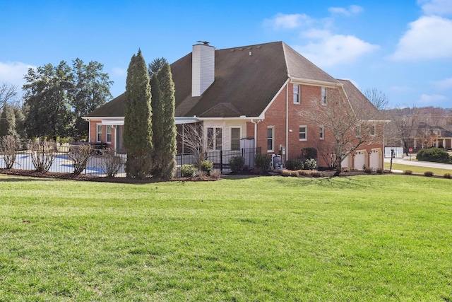 rear view of property featuring a garage, brick siding, fence, a yard, and a chimney