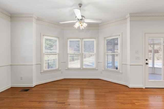 empty room featuring ceiling fan, a wealth of natural light, wood finished floors, and visible vents