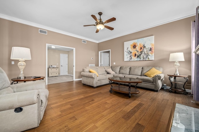 living room with a ceiling fan, visible vents, wood finished floors, and ornamental molding