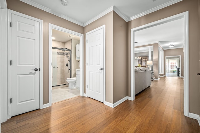 hall with light wood finished floors, baseboards, ornamental molding, and a chandelier