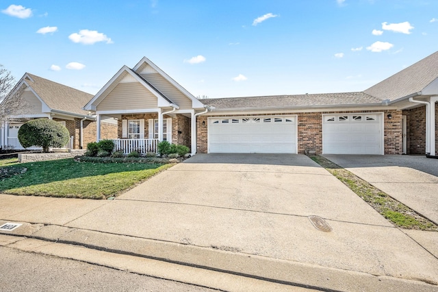 view of front of property featuring brick siding, covered porch, an attached garage, a front yard, and driveway