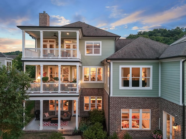 back of property at dusk featuring a balcony, a patio area, a chimney, and brick siding