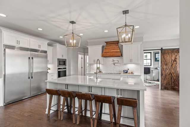 kitchen featuring built in appliances, a barn door, light countertops, custom exhaust hood, and decorative backsplash