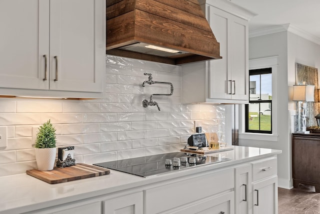 kitchen with crown molding, light countertops, custom range hood, decorative backsplash, and black electric cooktop