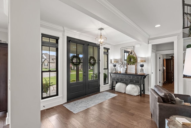 entrance foyer with visible vents, an inviting chandelier, ornamental molding, wood finished floors, and baseboards