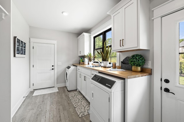 washroom with cabinet space, baseboards, washer and clothes dryer, light wood-style floors, and a sink