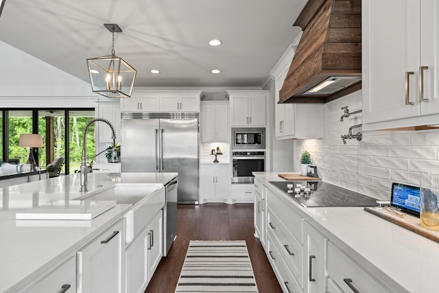 kitchen featuring white cabinets, dark wood-type flooring, decorative light fixtures, built in appliances, and custom exhaust hood