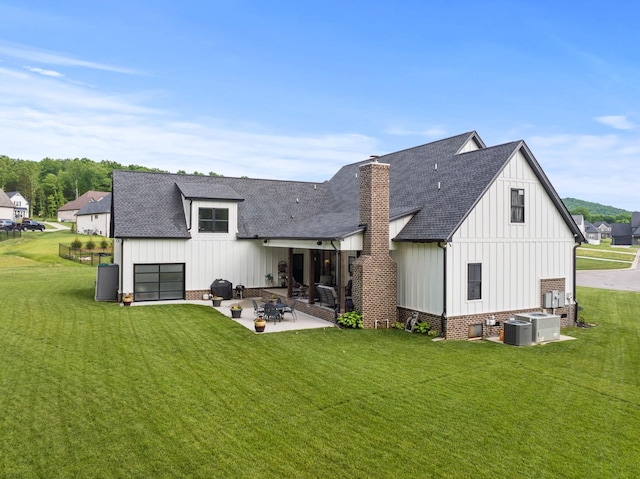 rear view of property featuring a yard, a chimney, a patio, a shingled roof, and board and batten siding