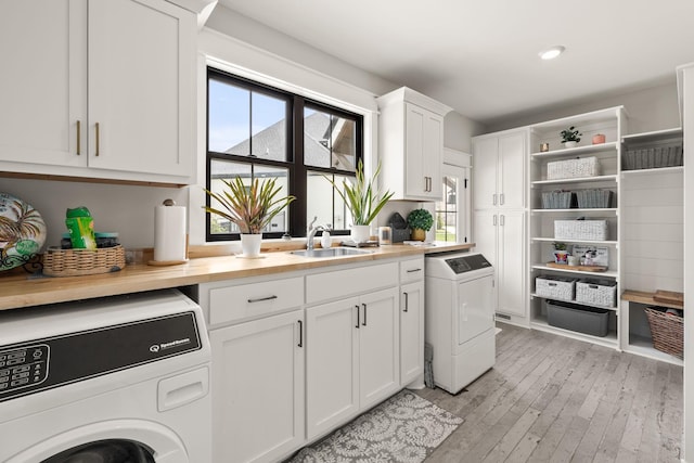 laundry area featuring cabinet space, a sink, light wood-style flooring, and separate washer and dryer