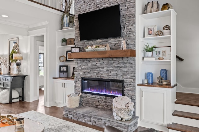 living area with built in shelves, dark wood-type flooring, a fireplace, stairs, and ornamental molding