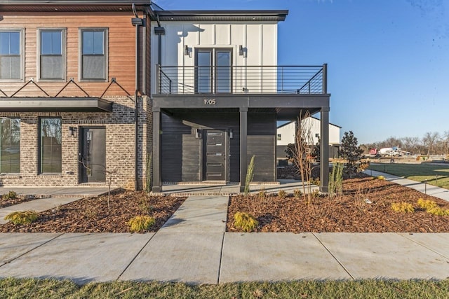 view of front of property with board and batten siding, brick siding, and a balcony