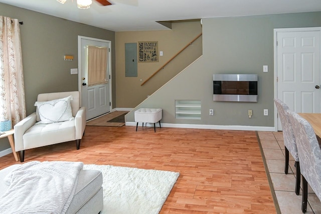 sitting room featuring light wood-style floors, ceiling fan, electric panel, baseboards, and stairs