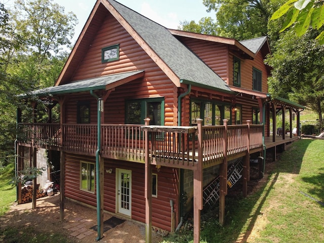 back of property featuring a deck, a patio, roof with shingles, a lawn, and log veneer siding