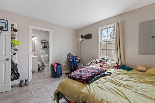 bedroom with light wood-type flooring, electric panel, and connected bathroom