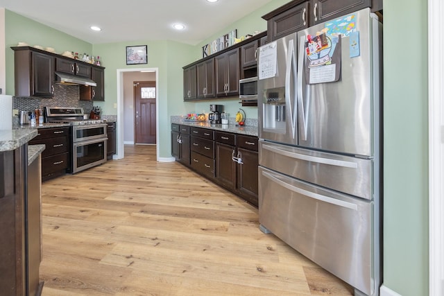 kitchen with stainless steel appliances, light wood-style flooring, decorative backsplash, dark brown cabinetry, and under cabinet range hood